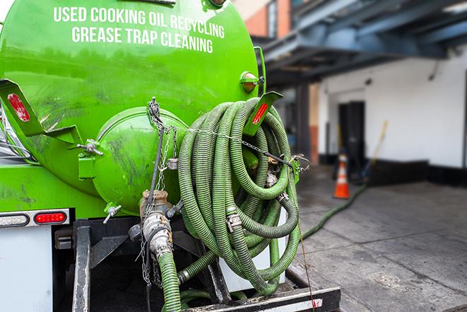 a professional plumber using a pump to empty a grease trap in Bremond